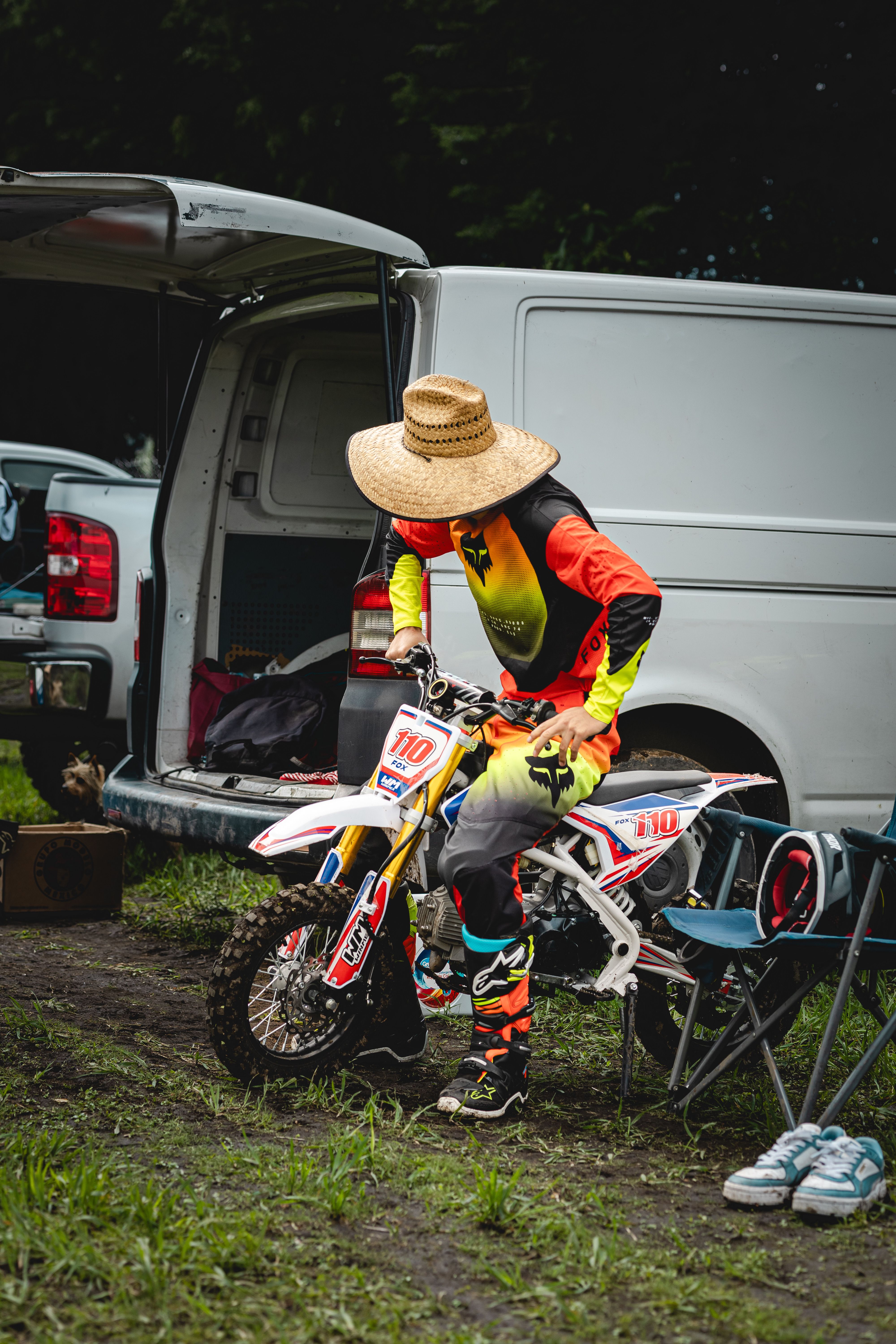 A motocross rider in colorful gear prepares for an outdoor bike event with a van in the background.