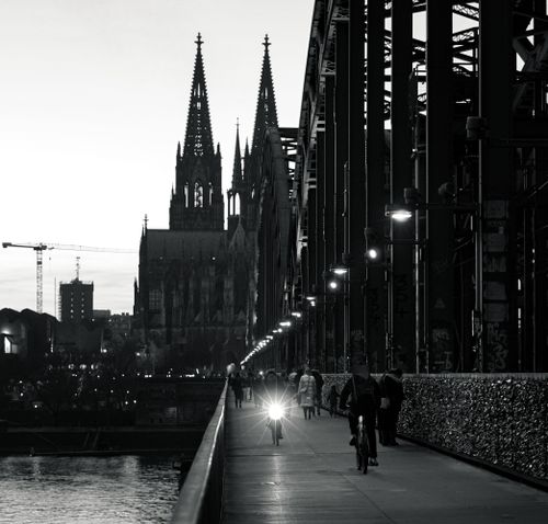 Free Black and white photo of Cologne Cathedral and Hohenzollern Bridge at twilight, featuring cyclists and pedestrians. Stock Photo