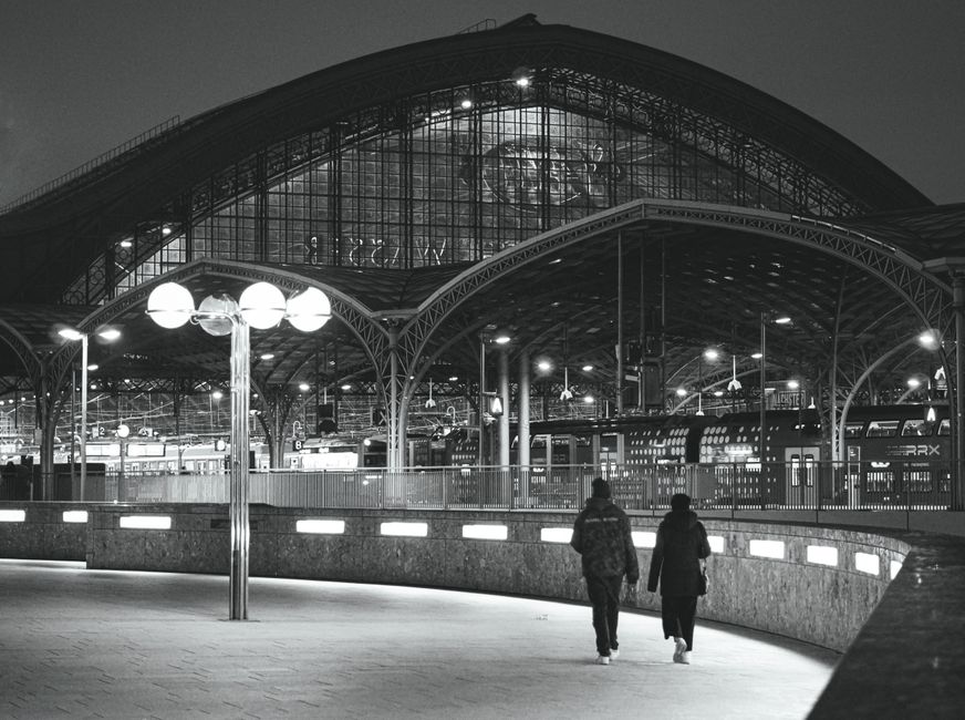 Two people walking towards Cologne Central Station at night, showcasing architectural beauty.