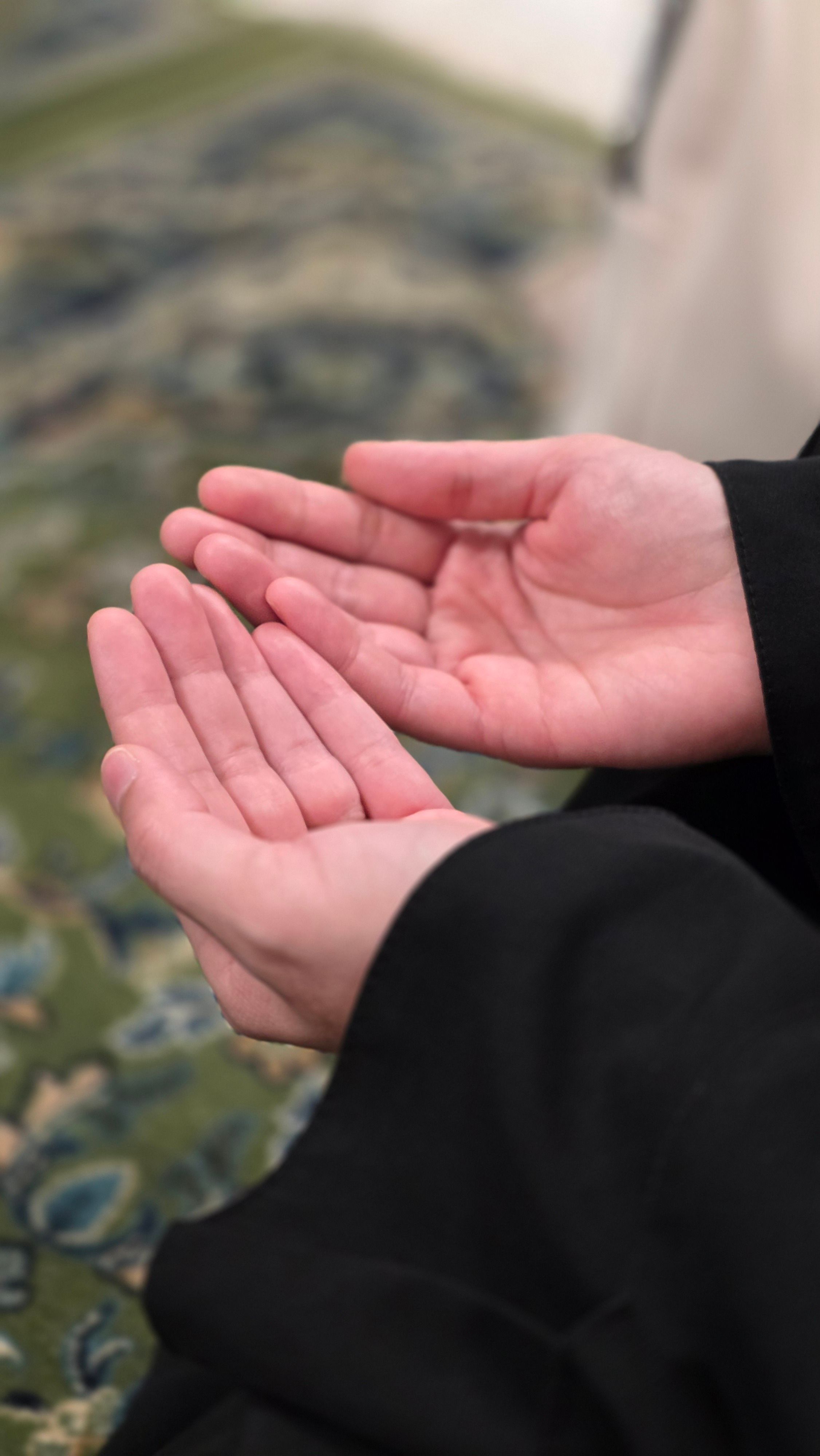 Close-up of hands in a prayer gesture on a patterned rug, depicting spirituality and meditation.