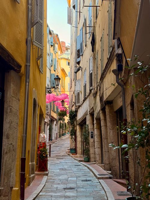 Free Delightful narrow street with colorful buildings and pink umbrellas in a European town. Stock Photo