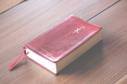 A red vintage-style Bible with ornate design lies on a wooden table, symbolizing knowledge and spirituality.