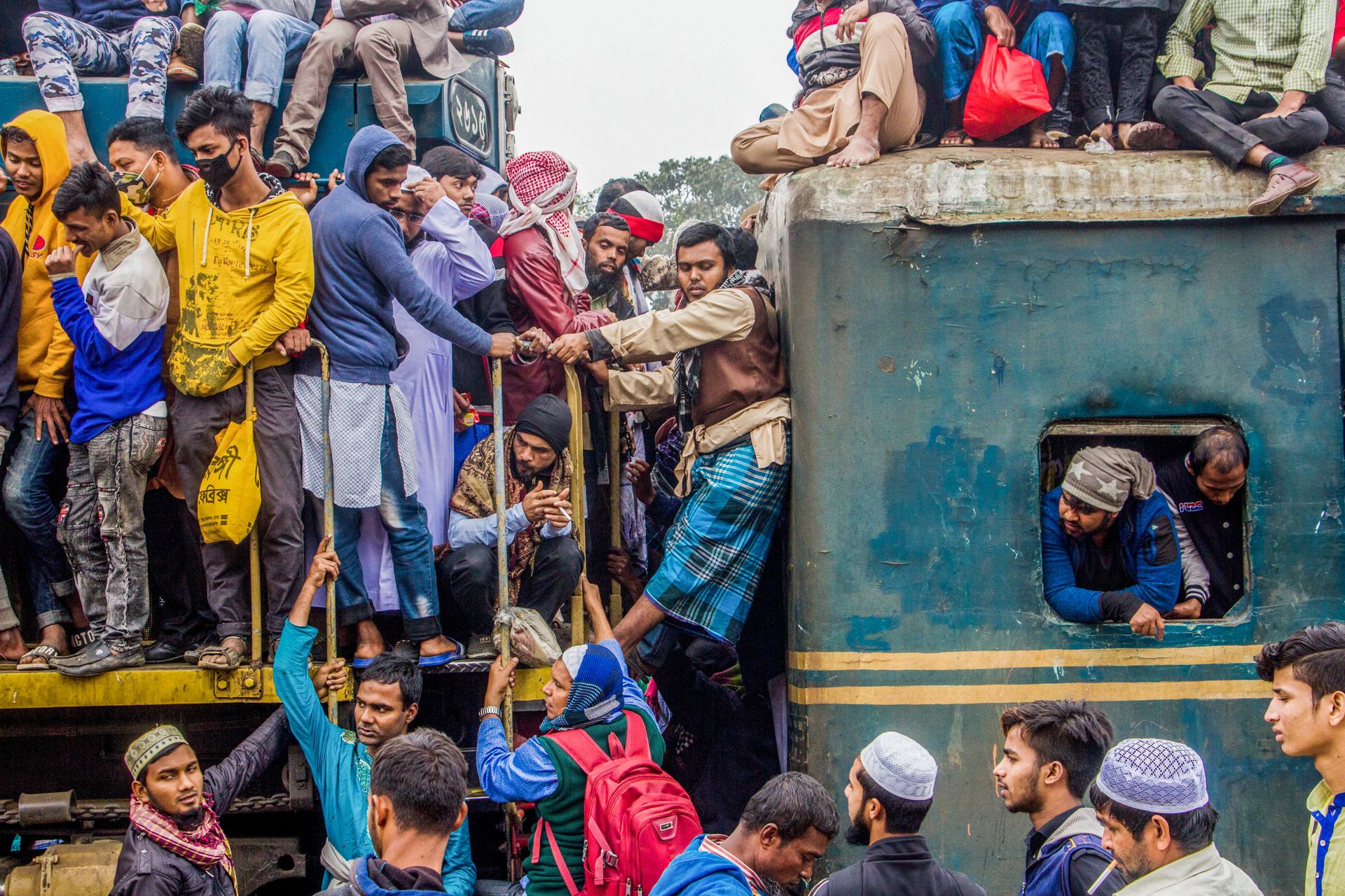 Overcrowded train with passengers traveling on the roof and sides, illustrating mass transit challenges.