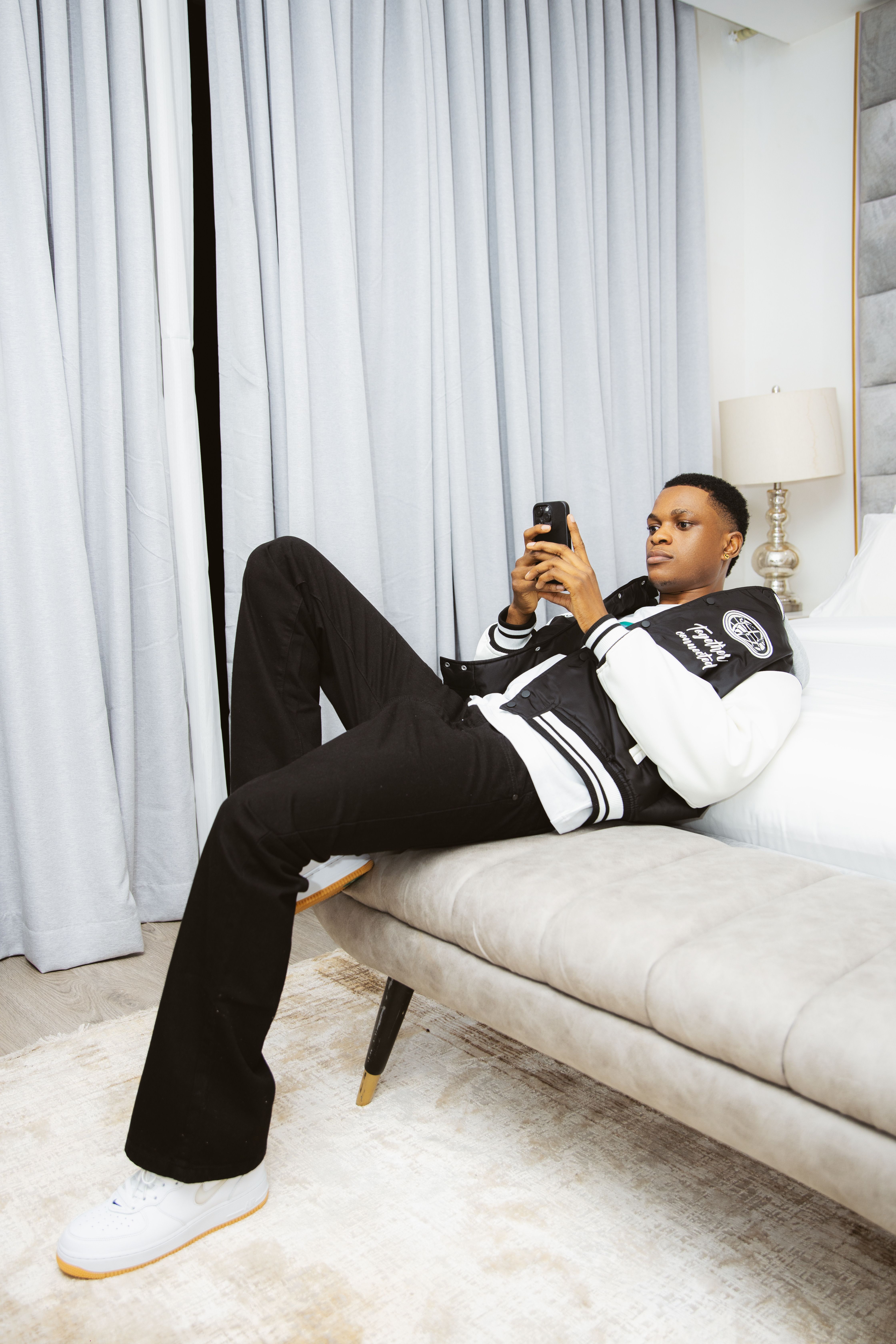 Young man in casual wear relaxing on a bench while using a smartphone indoors.