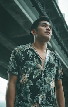 一位穿着花卉衬衫的时尚男子自信地在城市桥下摆姿势