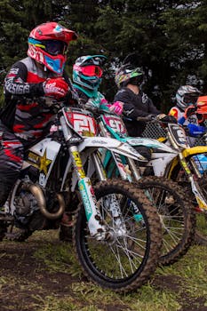 Motocross riders in colorful gear prepare to race on muddy terrain.