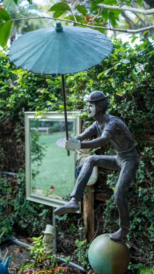 Free Outdoor sculpture portraying a playful figure with an umbrella in a lush garden setting. Stock Photo