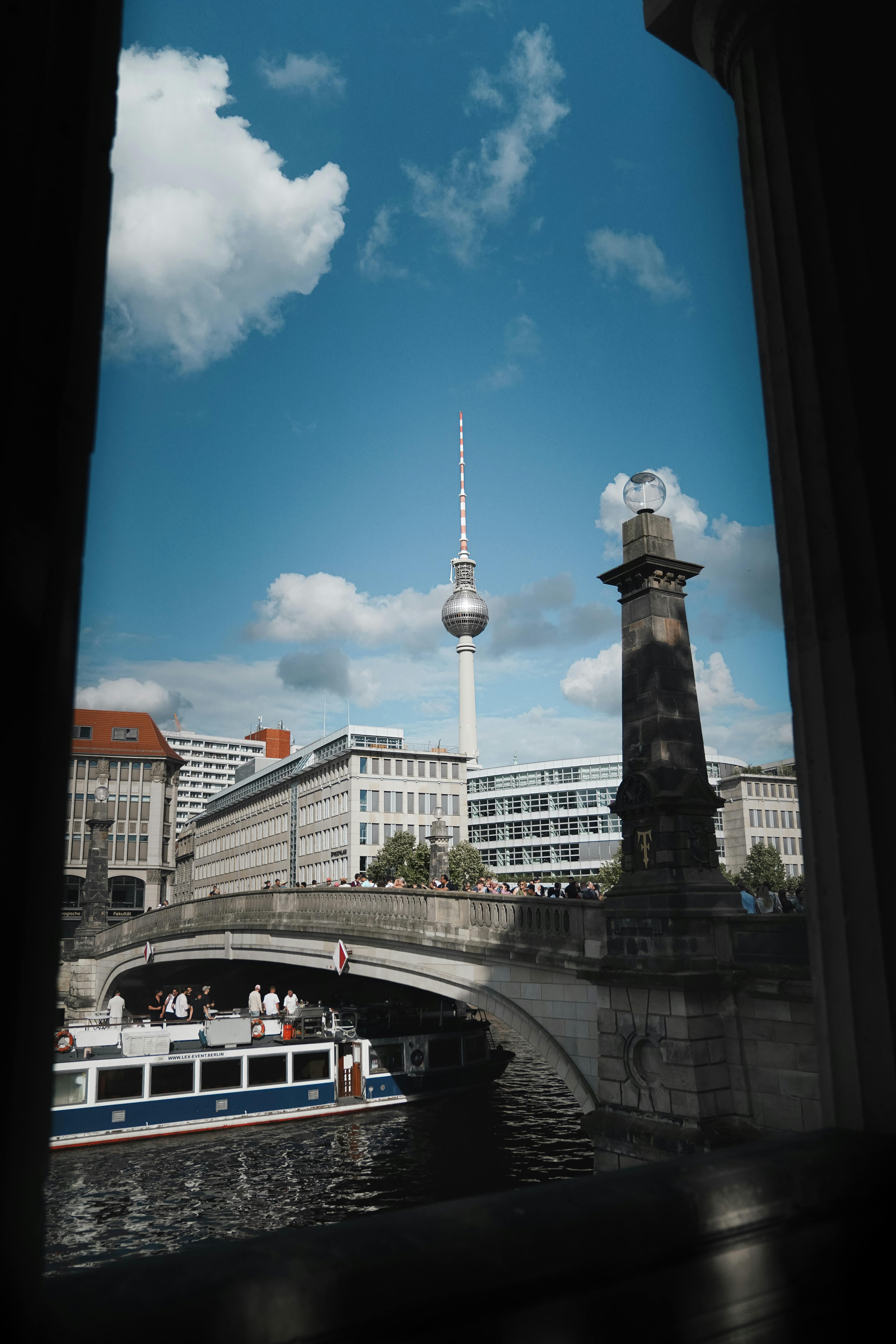A striking view of Berlin's TV Tower framed by an arch bridge and river, showcasing the city's modern architecture.