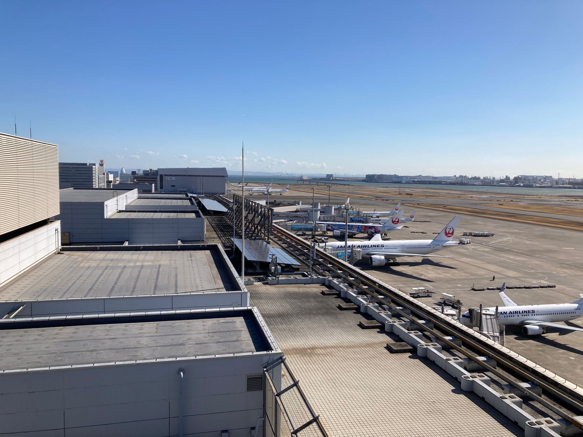 Aerial view of Haneda Airport with several airplanes parked at the terminal gates under clear blue skies.
