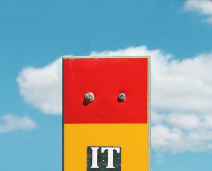 A red and yellow sign with 'IT' text under a bright blue sky with clouds in Helsinki.