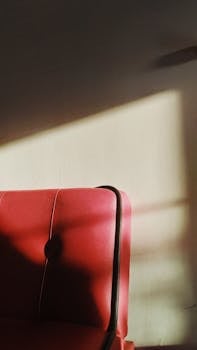 一把沐浴在自然阳光下的优雅红色皮革椅，置于极简主义设计的室内