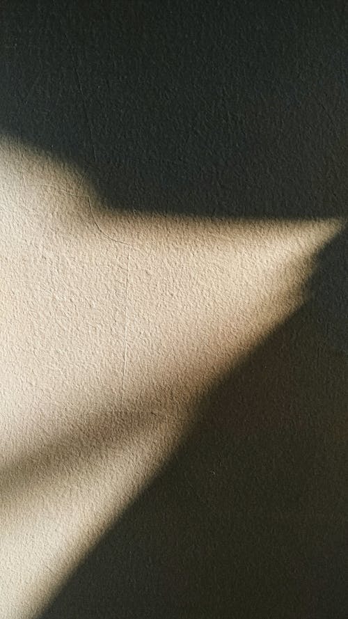 Sunlight from little part of window illuminating dark room with rough gray surface creating shadow on wall