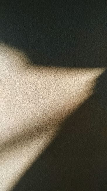 Sunlight from little part of window illuminating dark room with rough gray surface creating shadow on wall