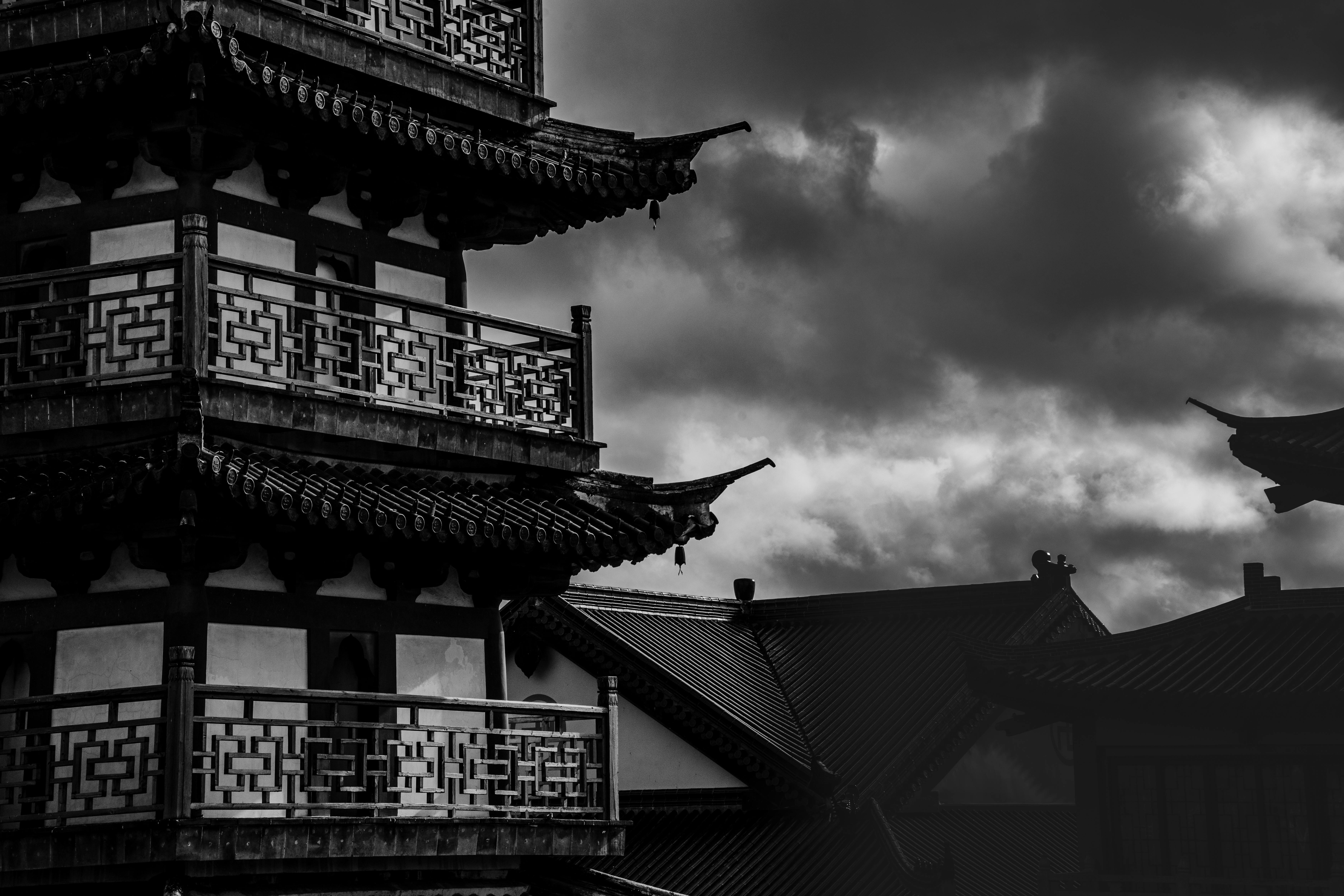 Black and white image of a traditional pagoda with dramatic clouds, showcasing architectural elegance and atmospheric tension.