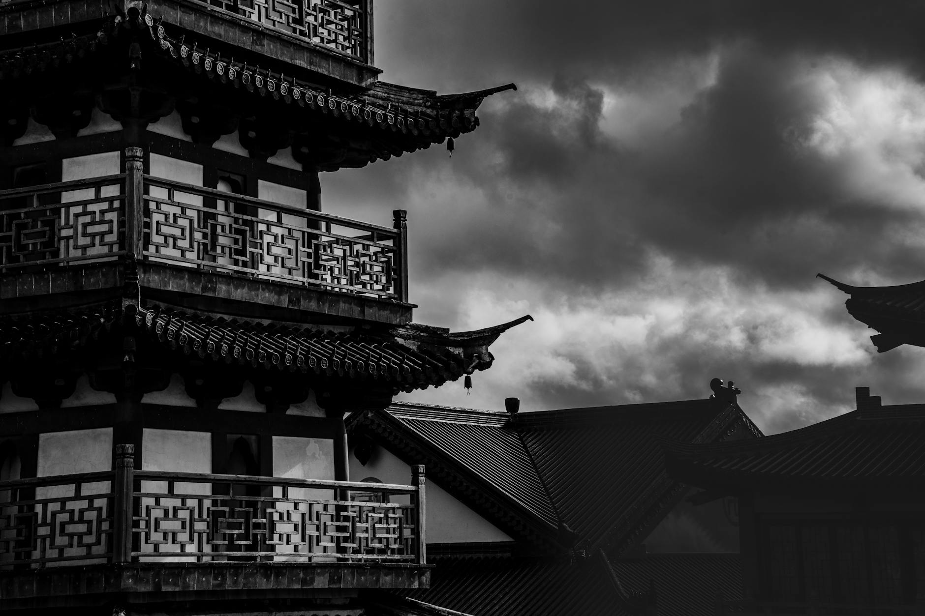 Black and white image of a traditional pagoda with dramatic clouds, showcasing architectural elegance and atmospheric tension.