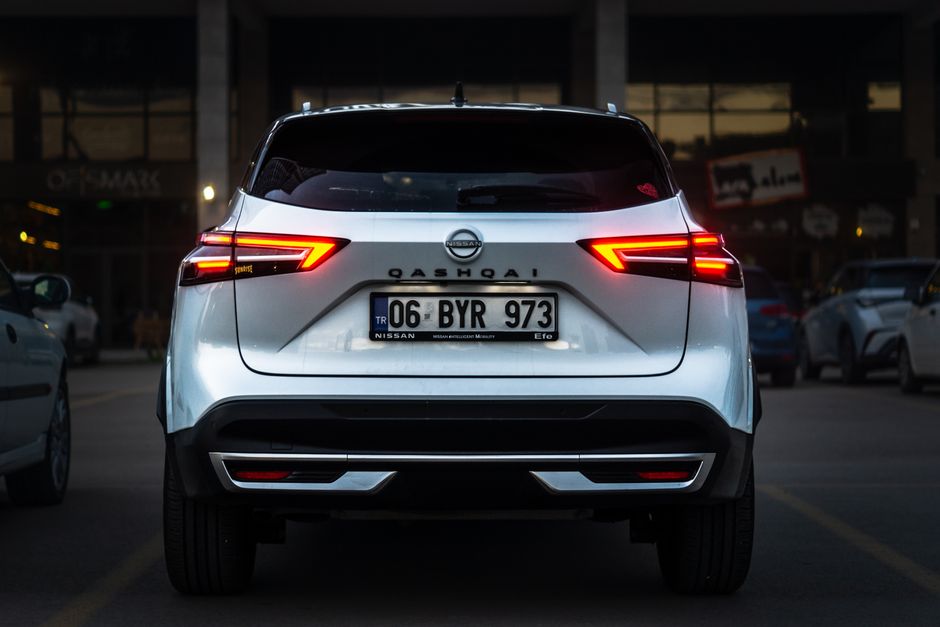 Nissan Qashqai with illuminated taillights parked in an urban area during twilight.