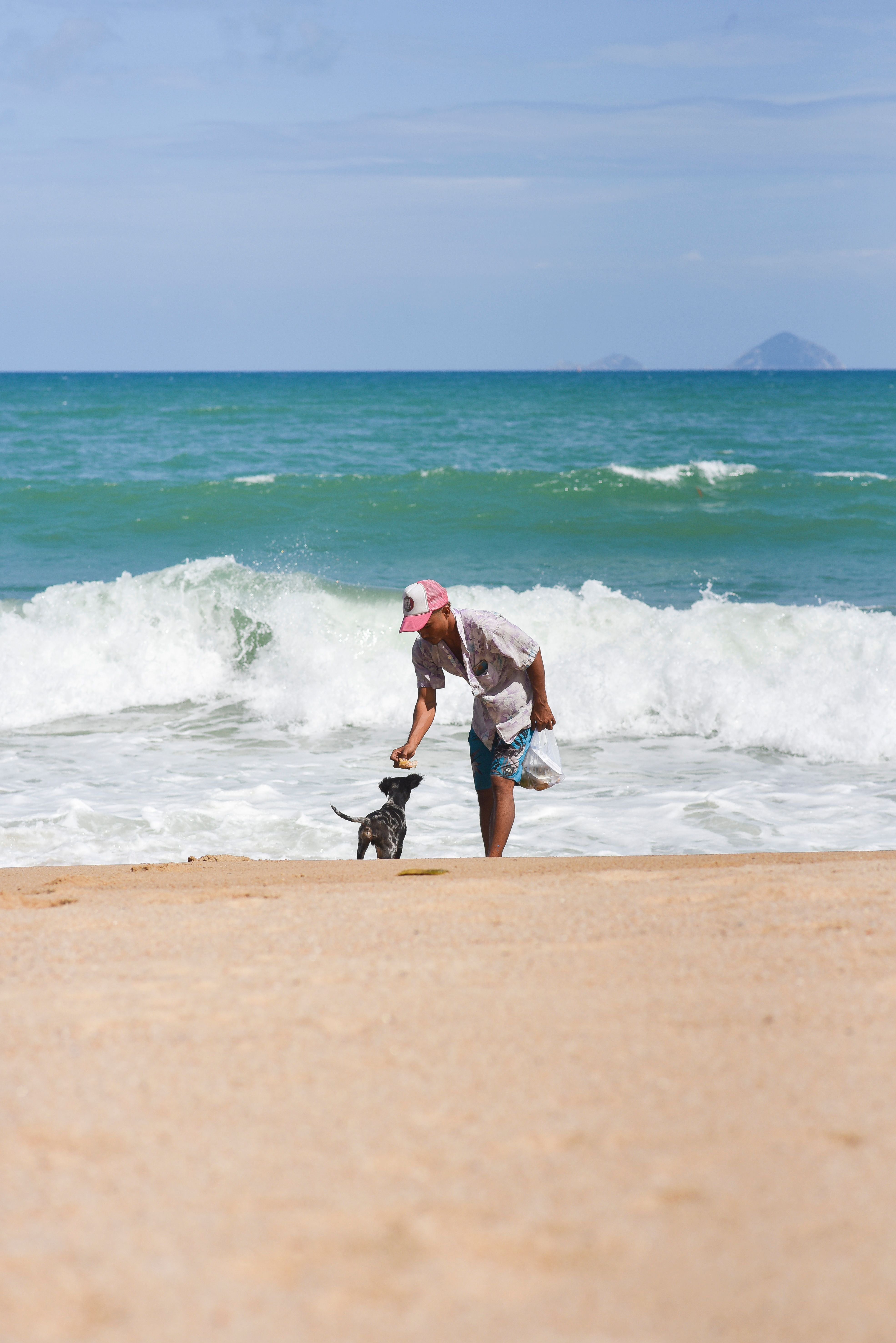 A man plays with a dog on the sandy beach of Nha Trang, Vietnam, under a clear blue sky.