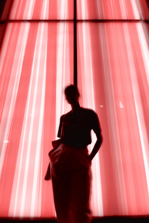 Женщина, стоящая у окна с розовой занавеской