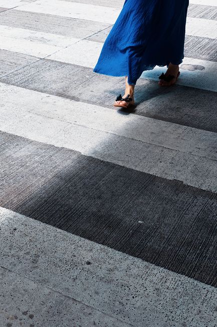 A woman in a blue dress walks across a crosswalk in an urban setting, capturing movement and fashion.