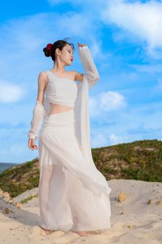 Graceful woman in white attire posing on a sandy beach under a bright blue sky.
