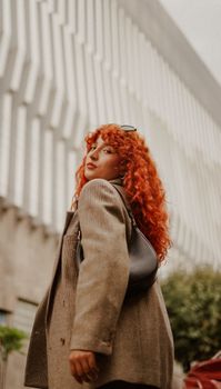 Stylish red-haired woman in a cityscape, exuding modern elegance and fashion sense.