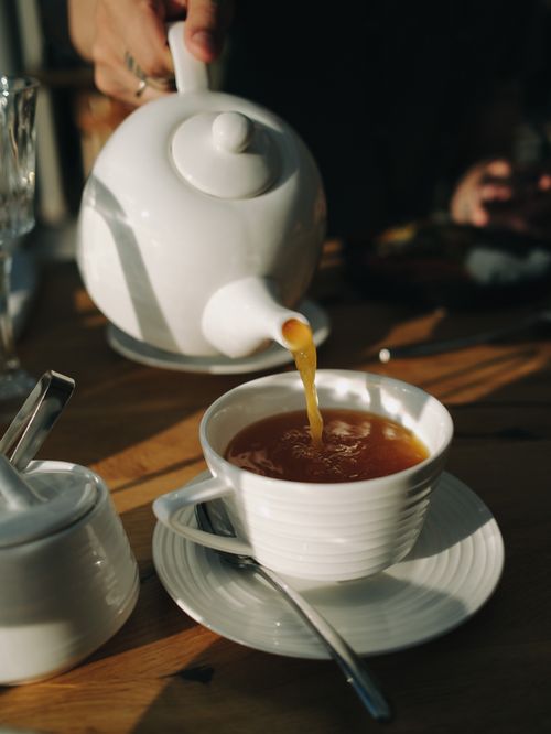 Free Elegant morning tea being poured into a white cup with natural light casting shadows. Stock Photo