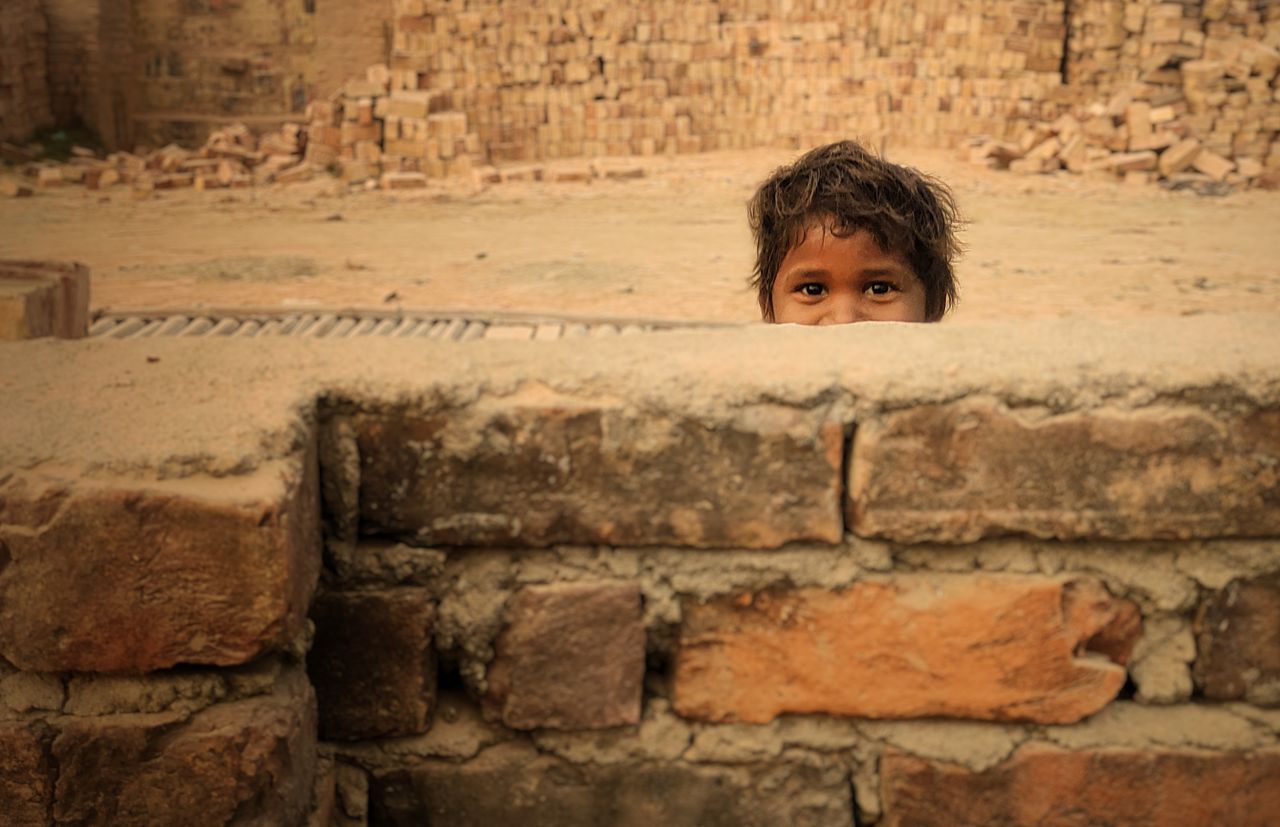 a young child peeks over a rustic brick wall in a construction site se