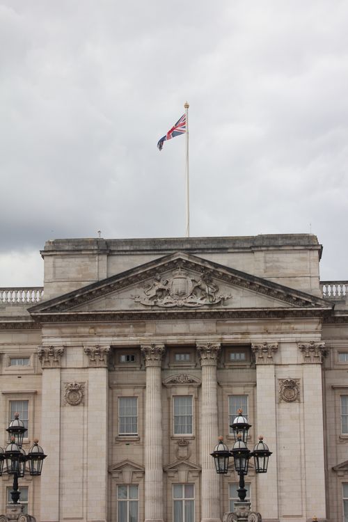 Free Front view of Buckingham Palace with British flag flying, cloudy sky overhead. Stock Photo