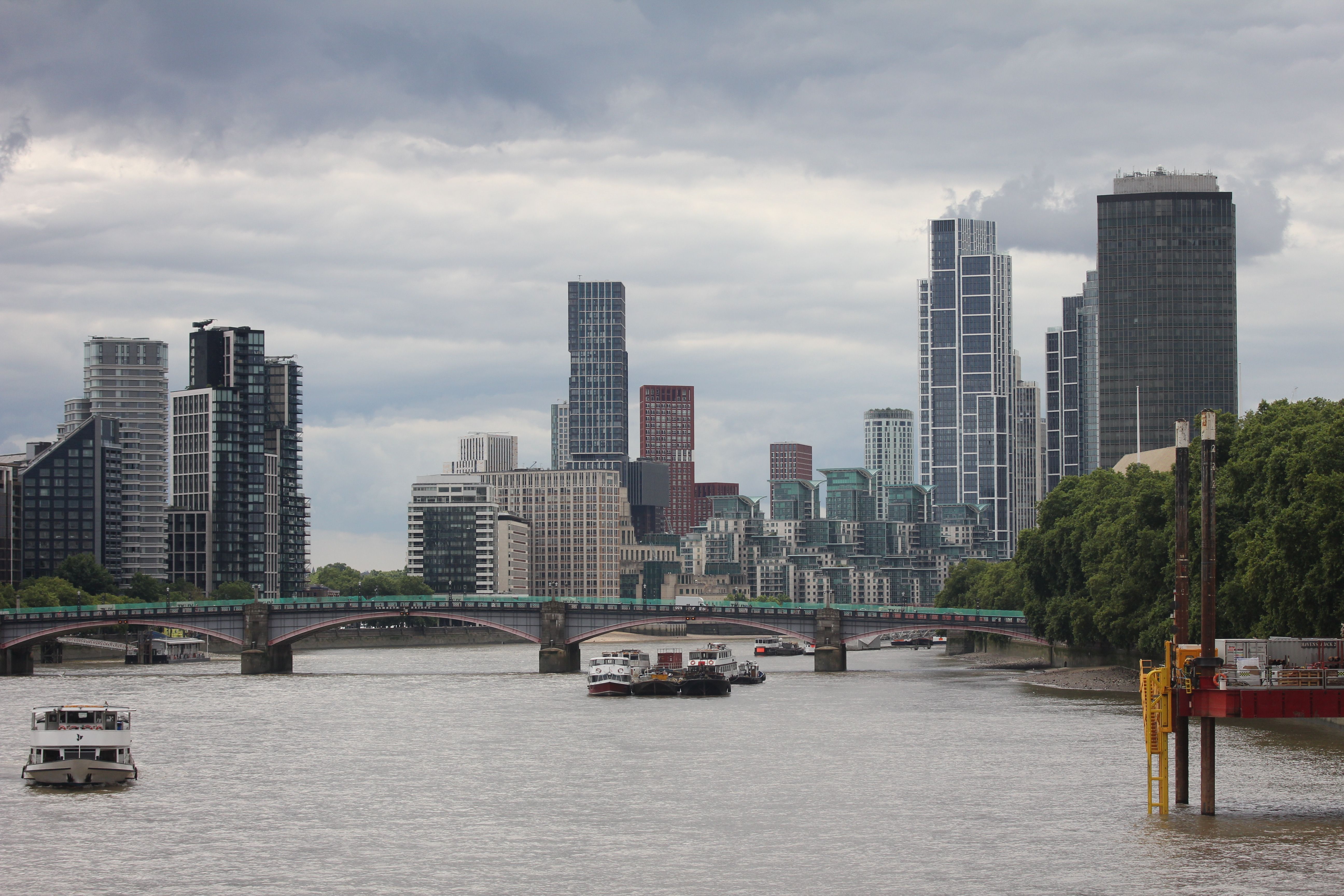 Impressive view of modern skyscrapers and bridge along River Thames in London under a cloudy sky.