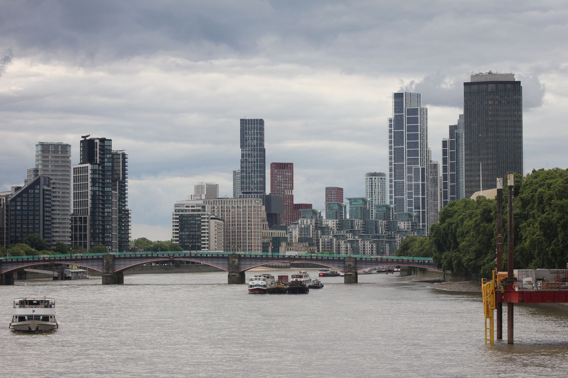 Impressive view of modern skyscrapers and bridge along River Thames in London under a cloudy sky.