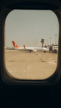 Looking out from an airplane window at an airport with a passenger plane and control tower.