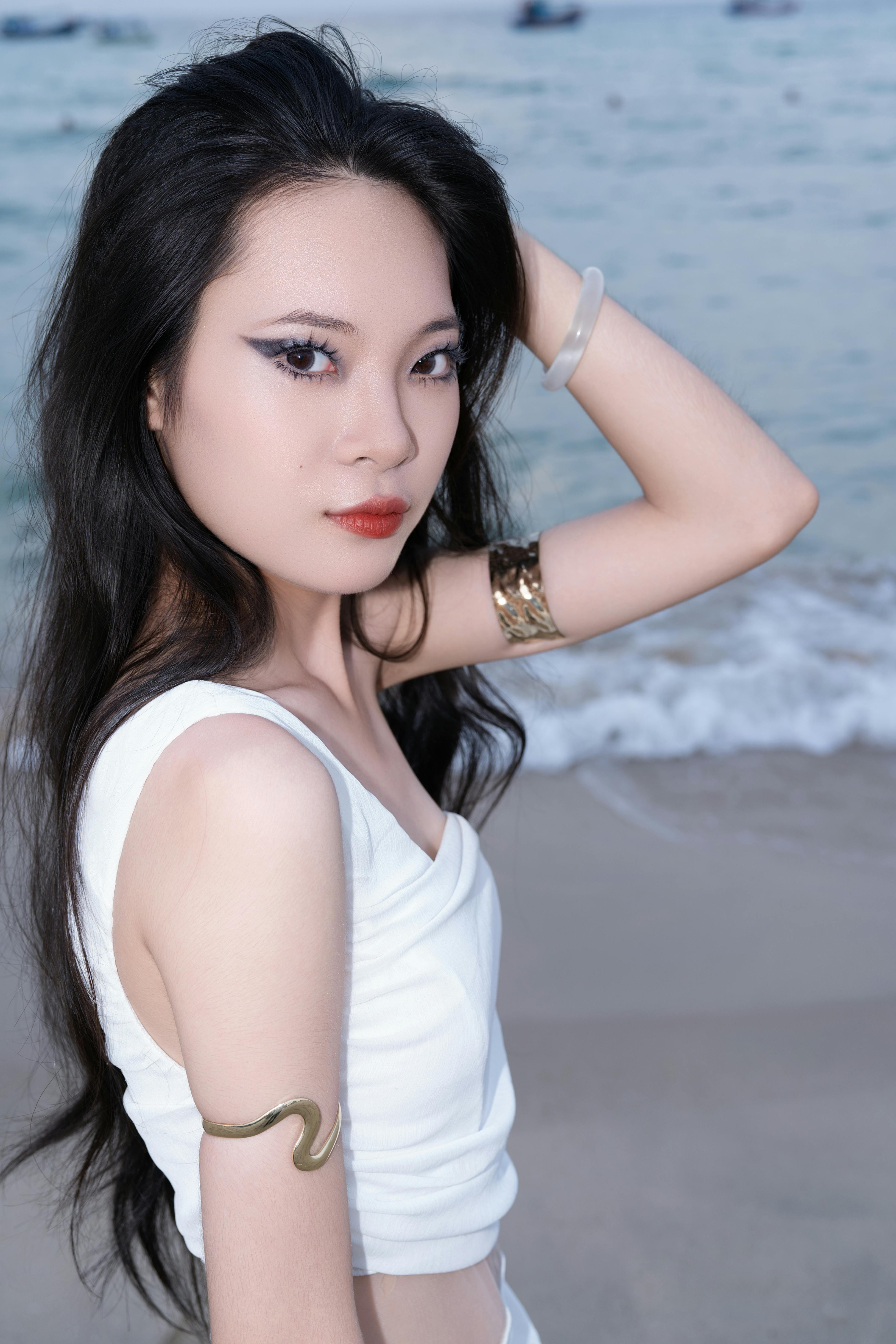 Stylish woman in white dress posing confidently on a beach during twilight.