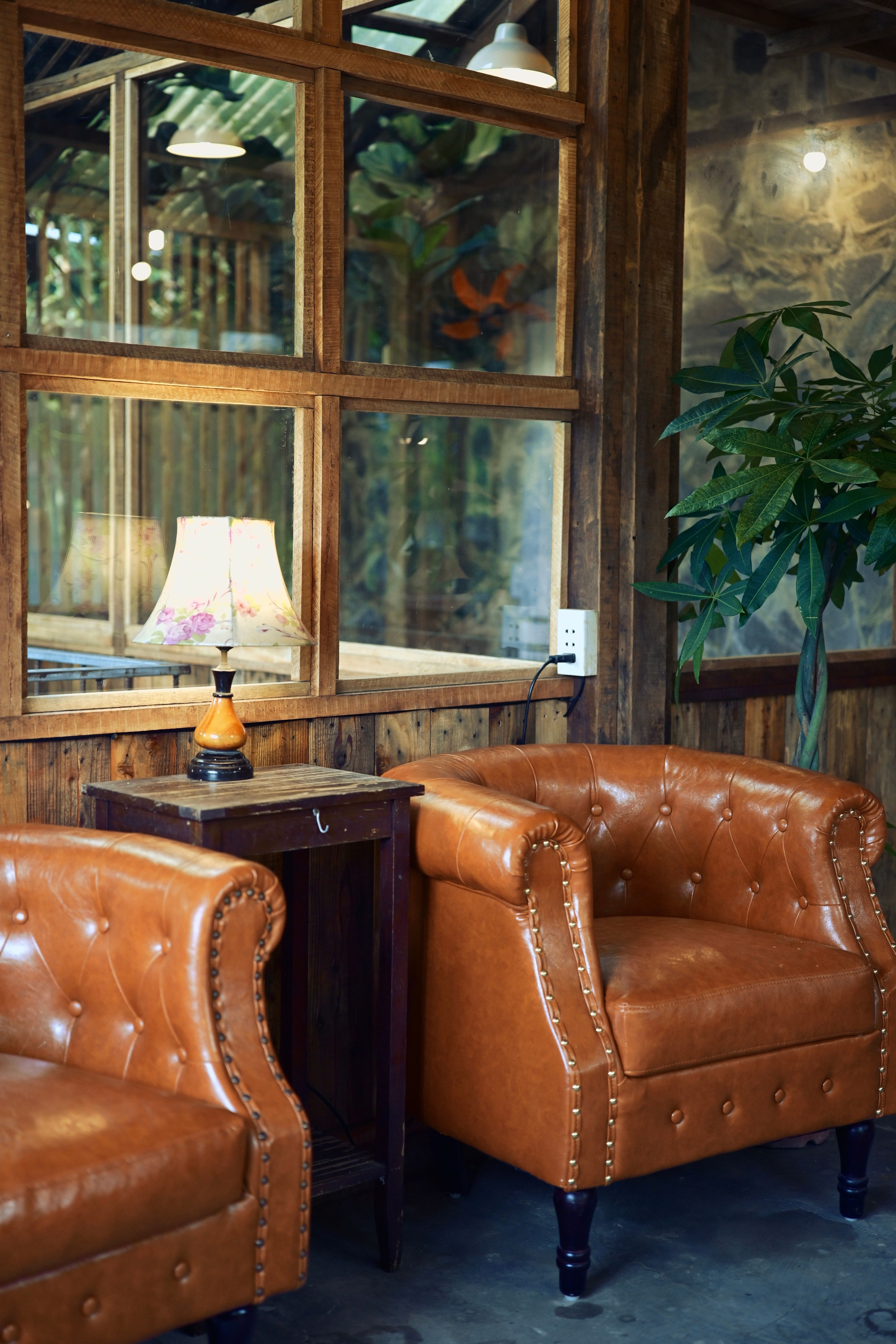 A cozy vintage indoor setting featuring leather chairs and a lamp by a wooden window.