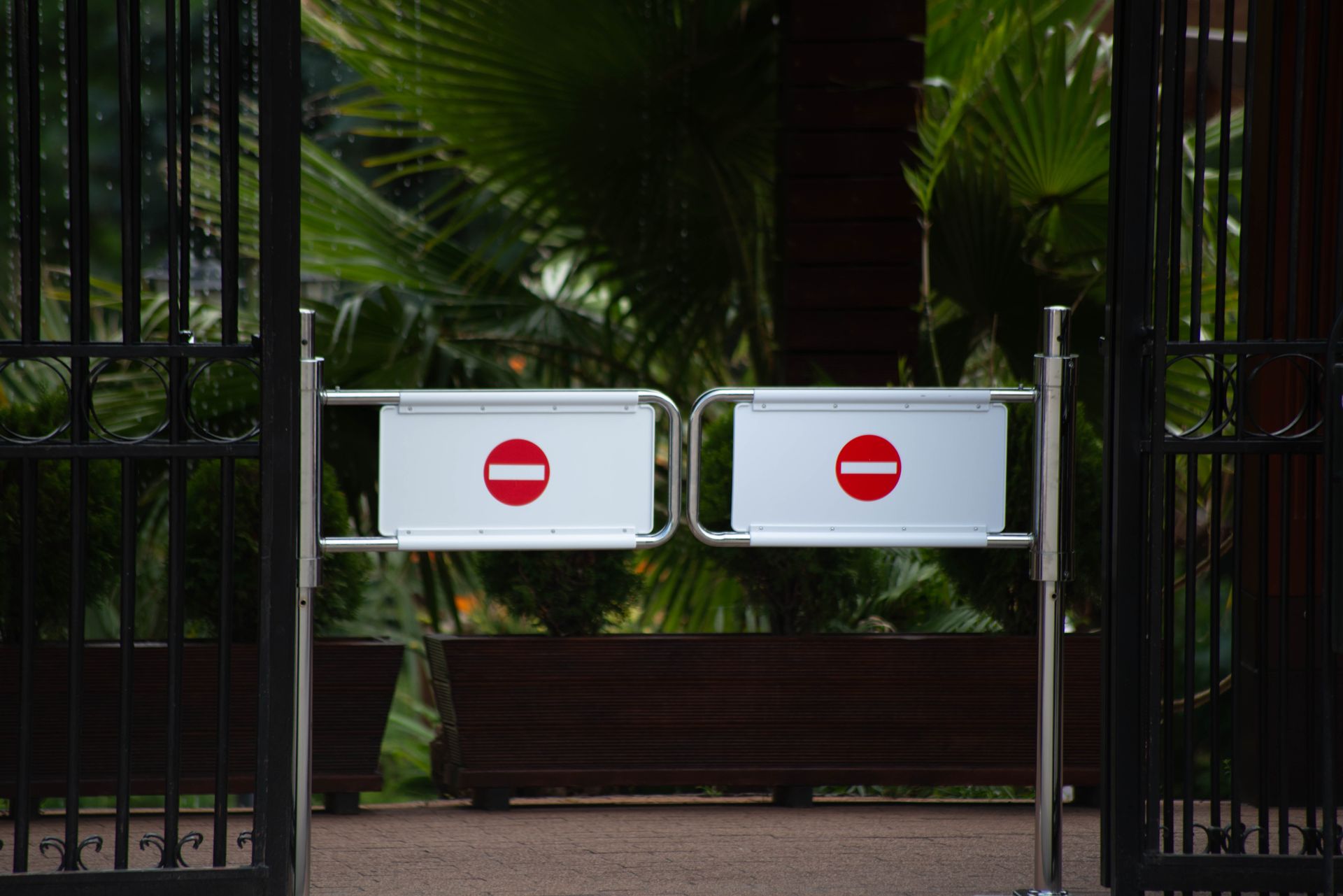 Metal gates with no entry signs at a lush garden entrance, conveying restricted access.