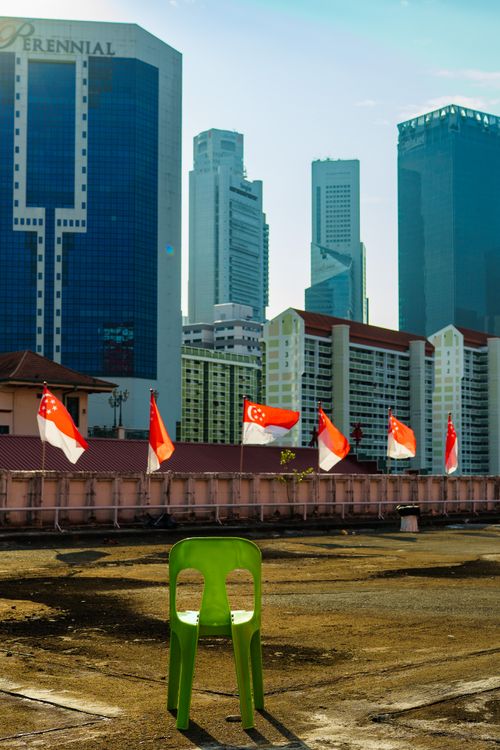 Free A lone green chair on a rooftop overlooking Singapore's skyline with national flags flying. Stock Photo