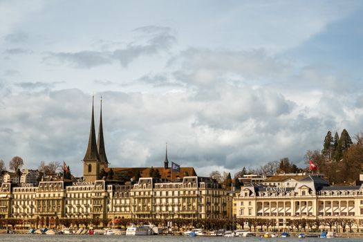 View of Lucerne's picturesque cityscape featuring iconic architecture, lake, and Casino Lucerne under a cloudy sky.