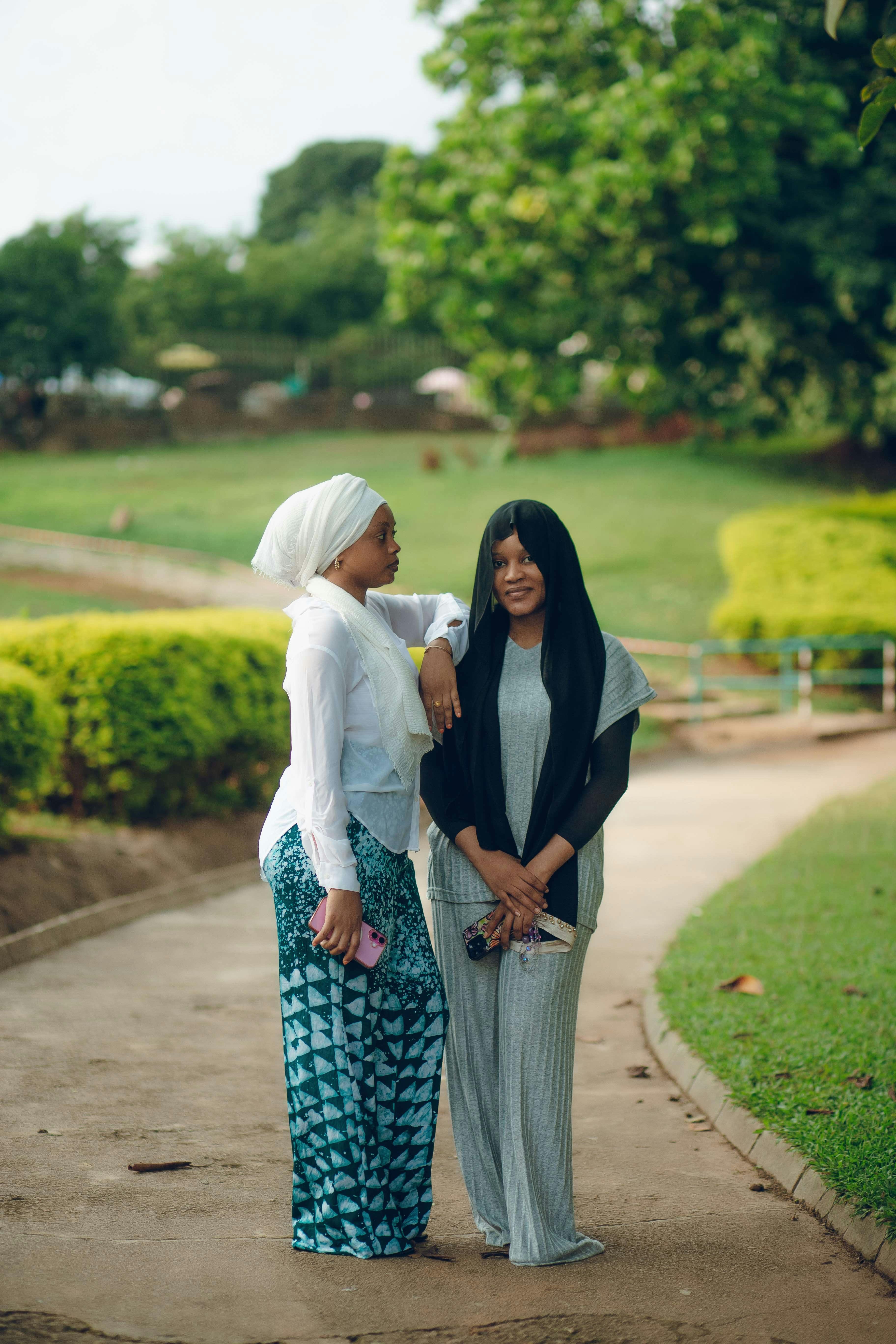 Two women engage in conversation in a sunny park, surrounded by lush greenery.