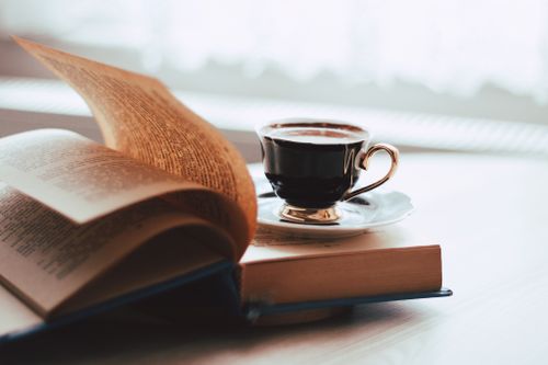 Free A cup of coffee beside an open book on a wooden table, creating a cozy reading atmosphere. Stock Photo