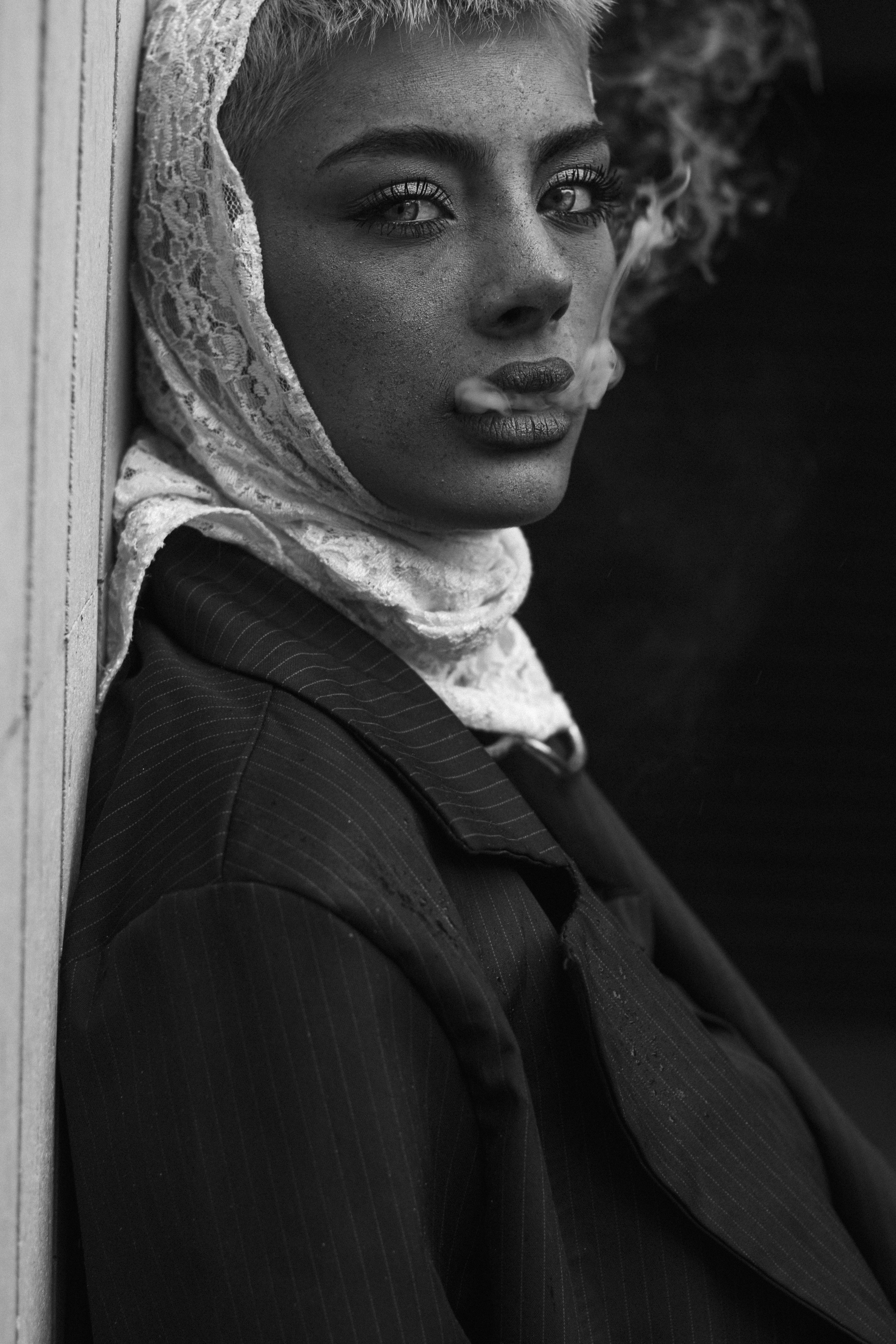 Dramatic black and white portrait of a woman smoking, featuring intense gaze and lace headscarf.