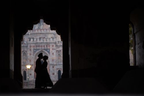 Free Silhouette of a couple embracing in front of an ancient archway at dusk, creating a romantic scene. Stock Photo