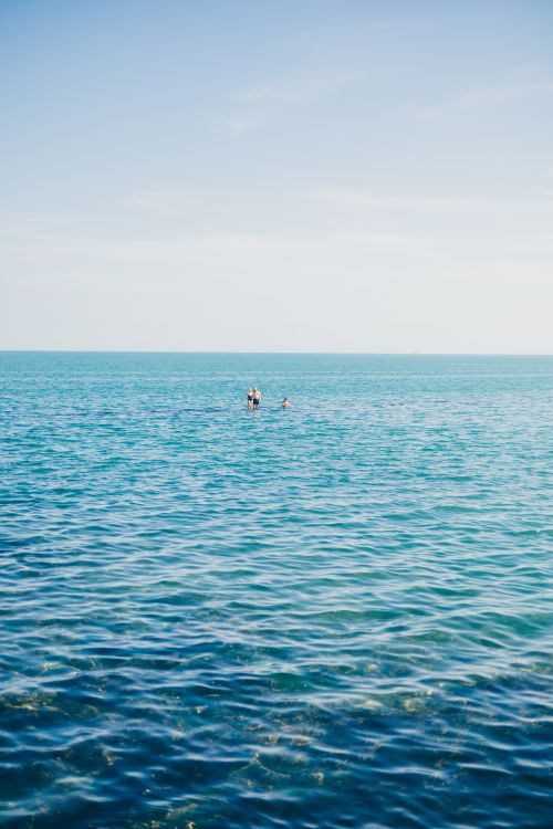 Free Two people swimming in the vast ocean under a clear blue sky, serene and peaceful. Stock Photo