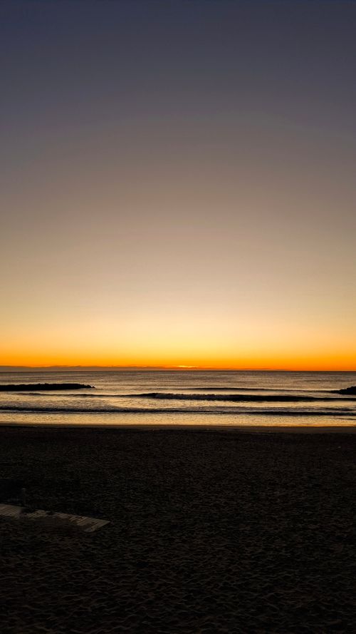 Free Serene sunrise view over Mar del Plata beach, Argentina, with calm waves and clear skies. Stock Photo