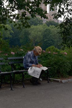 Elderly man reading a newspaper on a park bench in Central Park, NYC.