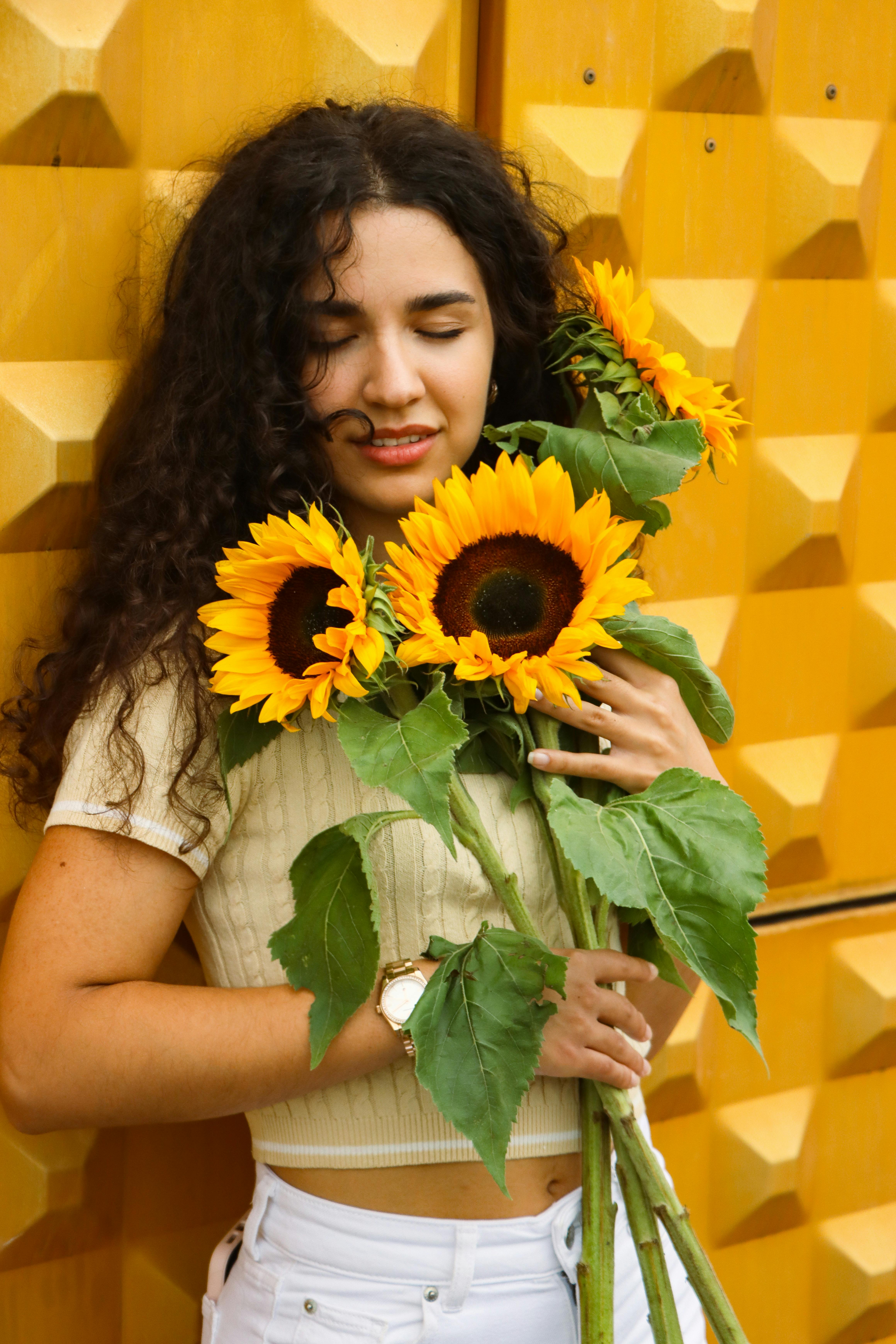 A young woman embraces sunflowers against a vibrant yellow background, capturing a moment of joy in Berlin.