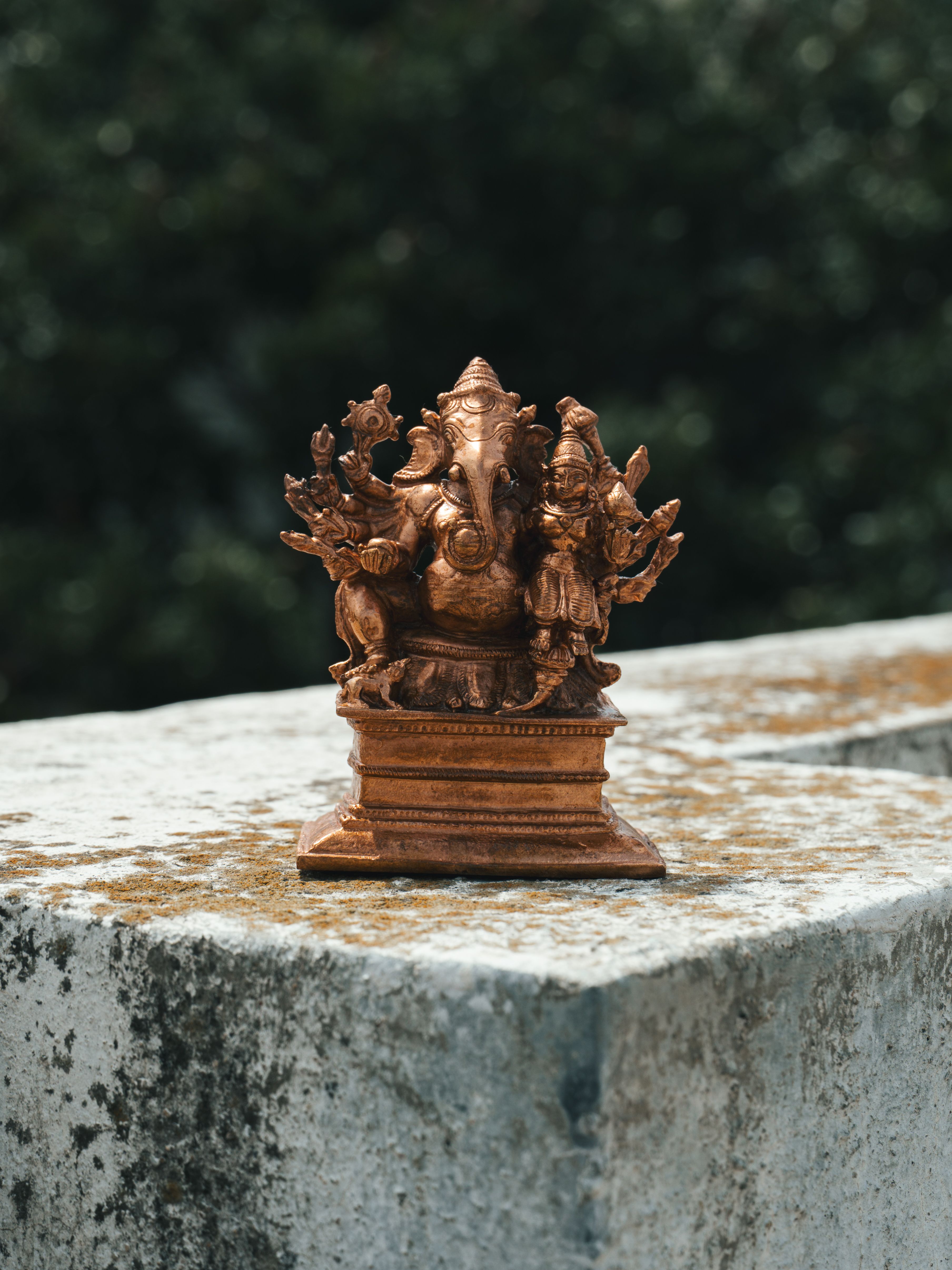 Close-up of a detailed bronze Ganesha statue placed on a textured stone surface.