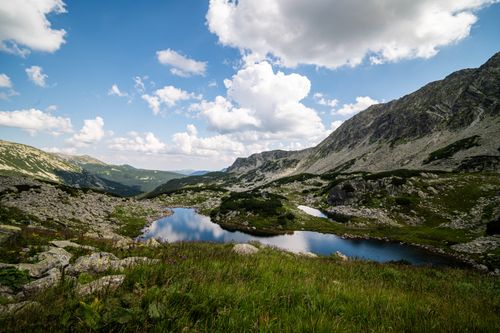 Free Peaceful alpine lake surrounded by rugged mountains under a vibrant blue sky, perfect for nature exploration. Stock Photo