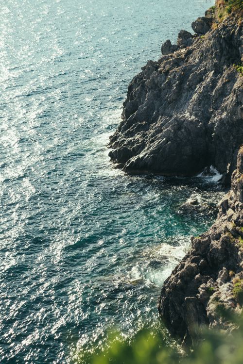 Free A breathtaking view of rocky cliffs meeting the shimmering ocean in Italy, perfect for travel inspiration. Stock Photo