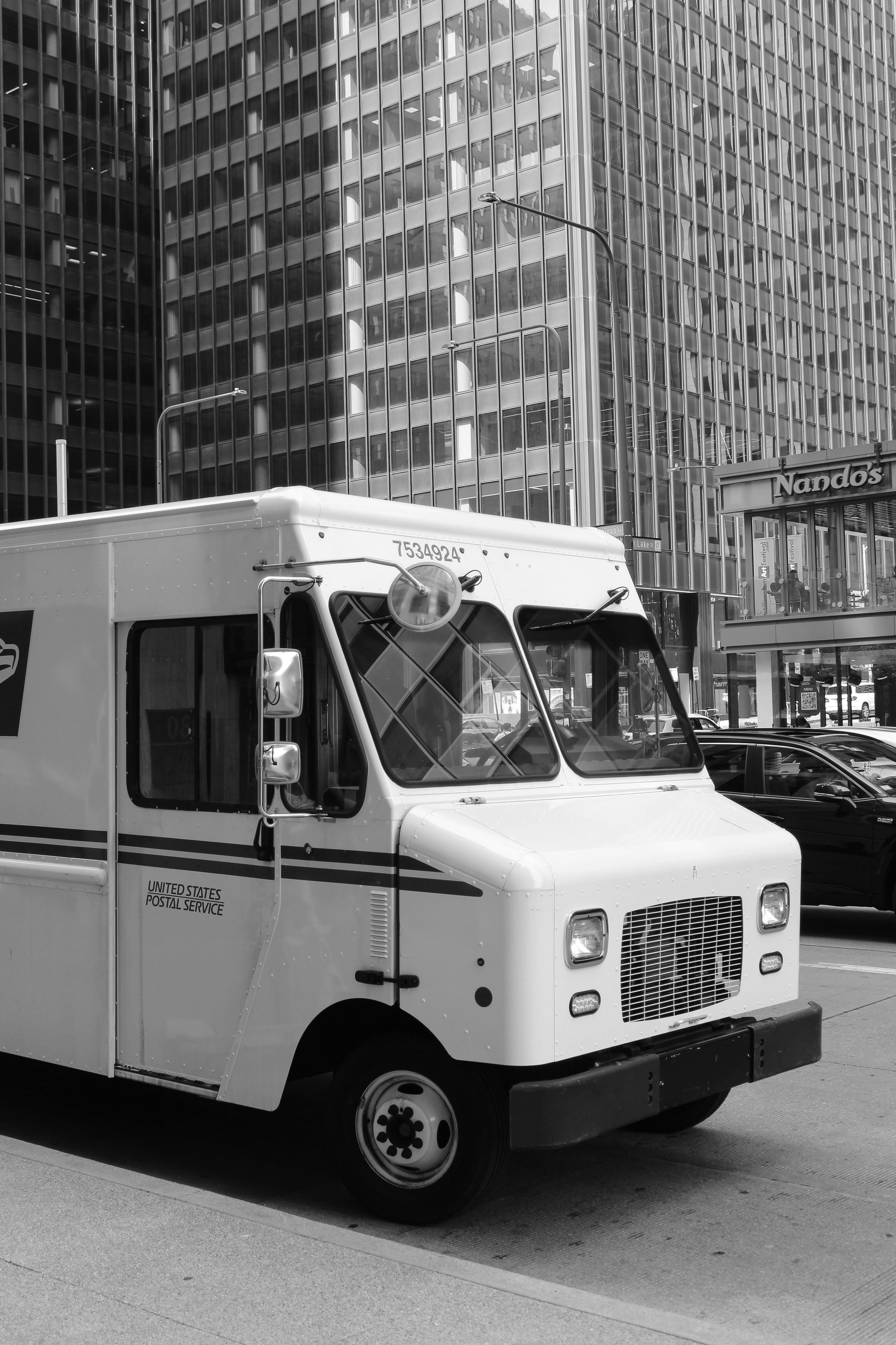 Black and white photo of postal truck amidst city skyscrapers.