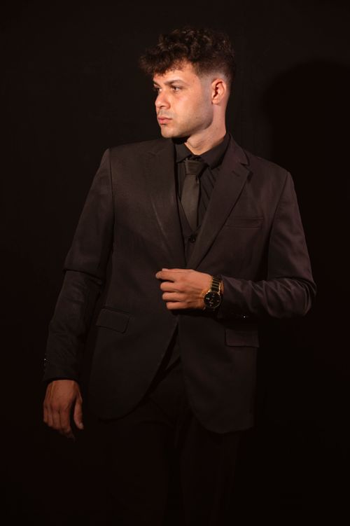 Free Portrait of a confident man in a dark suit against a black background, exuding elegance and style. Stock Photo