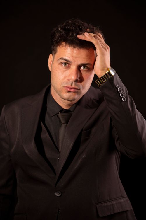Free Portrait of a stylish man in a black suit with a serious expression, touching his head. Stock Photo